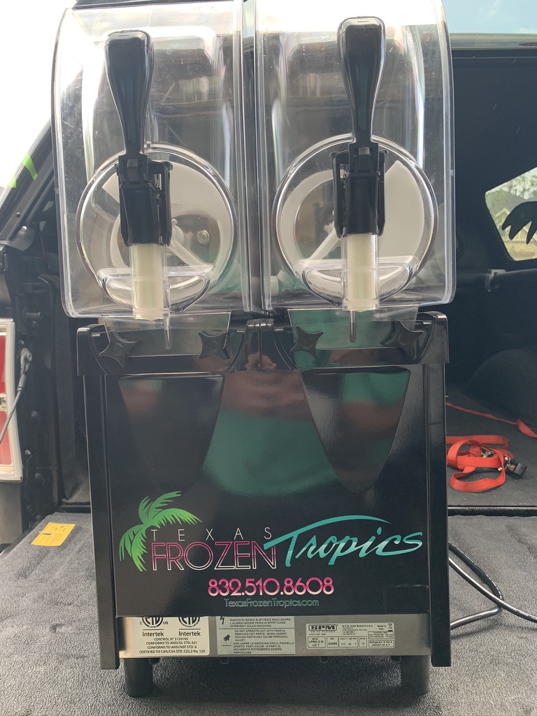 Close-up of a Texas Frozen Tropics branded frozen drink machine with logo and phone number